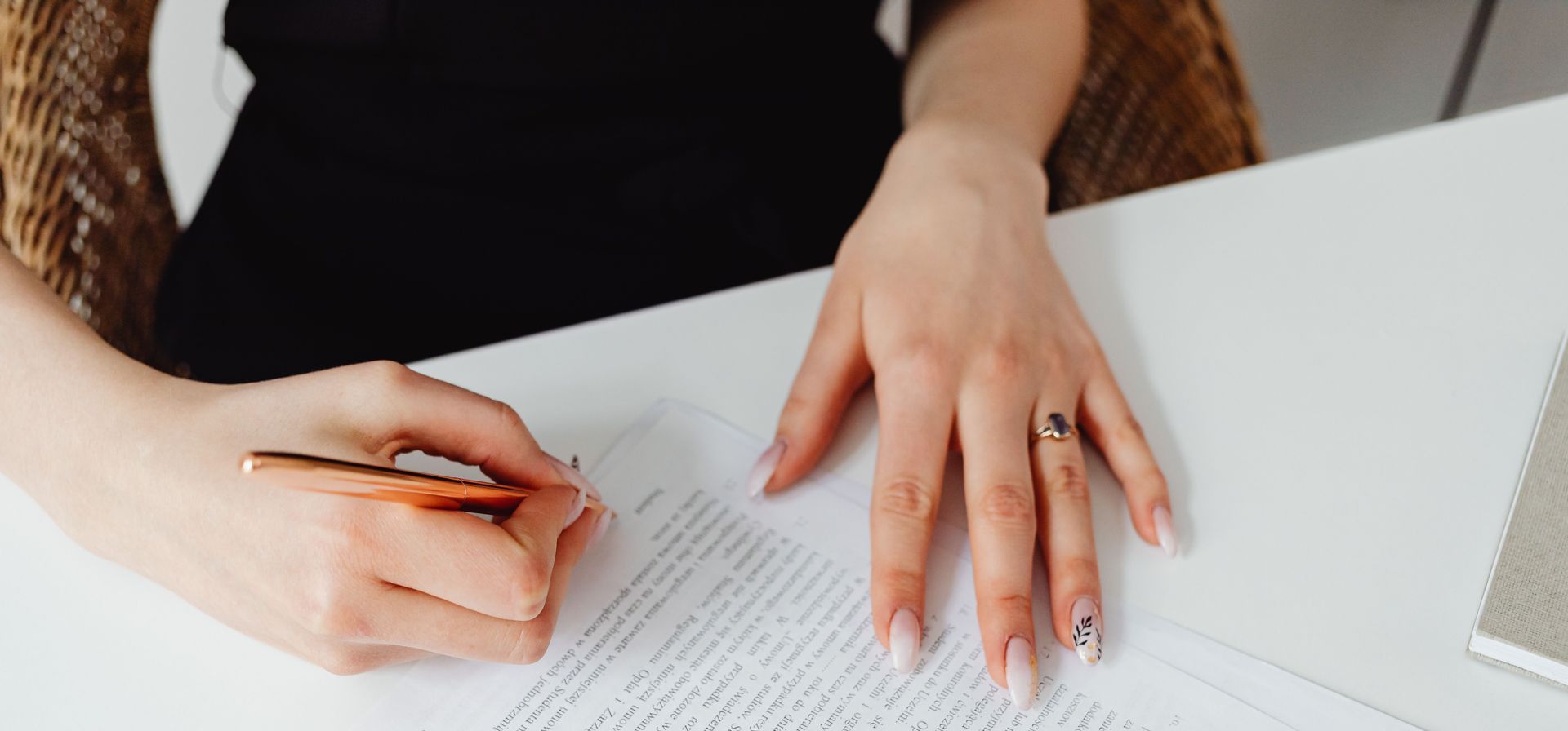 A woman signing a document with a pen on a desk, emphasizing hands and writing.